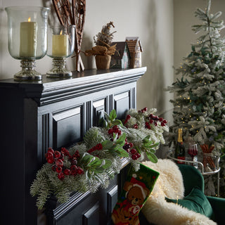 Red berry stems incorporated into a frosted Christmas garland on a black mantelpiece in a festive room setting.