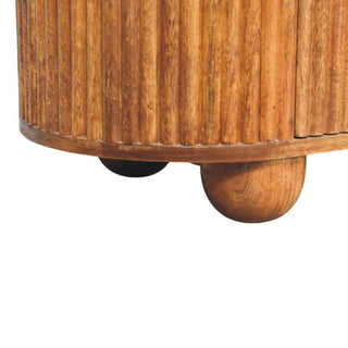 Detail of the amber oak chest showing the ridged texture wrapping the rounded base and spherical feet.