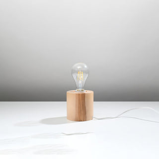 Angled view of the cylindrical natural wood lamp base, showing the grain and the white power cord trailing across the surface.