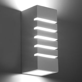 Angled view of the illuminated ceramic wall lamp showing bright light spilling from the five horizontal openings.