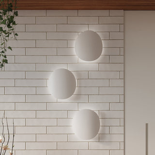 Three asymmetrical white wall lights mounted vertically on a white tiled wall, showing the soft illuminated halo.