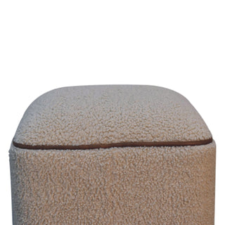 Close detail of the beige boucle fabric texture and the brown piping seam on the footstool.