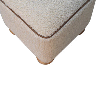 Detail shot of the footstool corner showing the boucle upholstery, brown piping, and the placement of two wooden ball feet.
