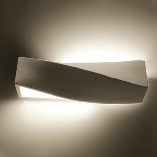White ceramic lamp showing the dramatic shadow line created by the wavy form against the illuminated wall.