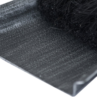 Extreme close-up of the textured silver dustpan surface and black brush bristles.