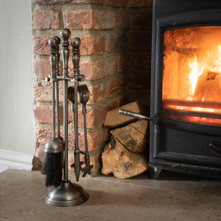 Silver nickel tool set on a stone hearth next to a lit wood-burning stove and exposed brickwork.