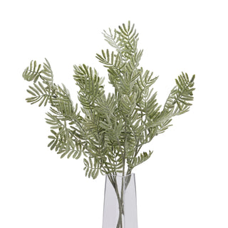 Multiple artificial silver wattle stems displayed upright in a tall, clear glass vase against a white background.