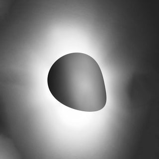 Asymmetrical wall light fixture shown in silhouette, producing a bright halo of light against a dark wall.