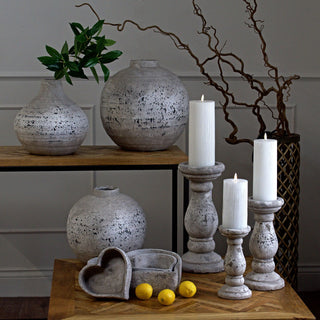 Grouping of three stone-effect ceramic pedestal candle holders of different heights on a wooden surface.