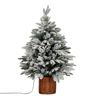 Flocked artificial fir tree in a brown rattan pot, shown front-on against a white background. A power cord trails to the left.