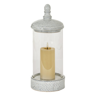 Grey speckled ceramic and glass lantern holding a lit cream pillar candle.