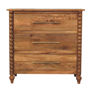 Front view of the mango wood three-drawer chest with spindle sides, brass bar handles, and turned feet.