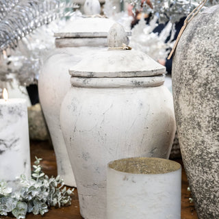 Styled scene showing the white ginger jar on a wooden surface surrounded by a lit candle and silver festive decor.