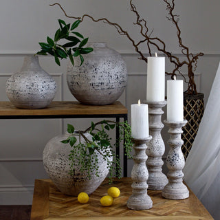 Three column candle holders arranged on a wooden surface with vases and greenery in a styled interior shot.