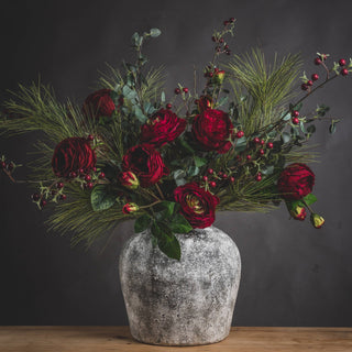 Aged stone effect vase filled with dark red faux flowers, green pine foliage, and red berries.