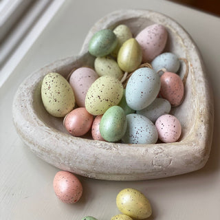 Vintage cream stone heart bowl holding colourful speckled decorative eggs.