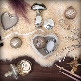 Styled shot showing the heart bowl holding small ornaments, placed on a light sheepskin throw.