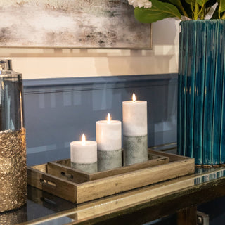 Three glowing stone effect LED candles in a gold tray on a reflective console table, next to a tall, ribbed teal vase.
