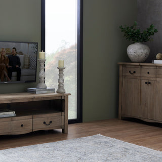 Pair of stone pillar candle holders on a wooden media unit in a room with dark green walls.