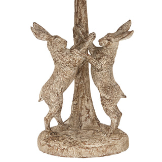 Detail of the stonewashed lamp base showing two boxing hares standing upright against a central tree trunk.