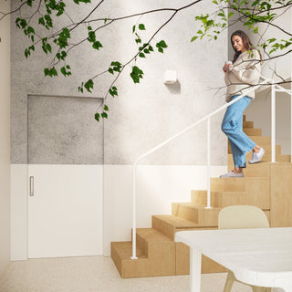 Wall lamp mounted on a textured wall in a modern interior with wooden stairs and green foliage.