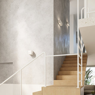 Pair of ceramic wall lamps installed vertically on a grey pillar beside wooden stairs and white railings.