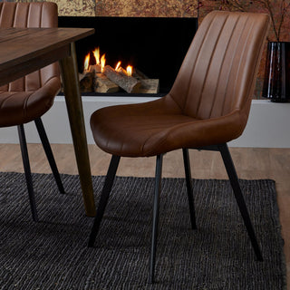 Tan faux leather dining chair set beside a dark wood table in a room with a lit fireplace and dark rug.