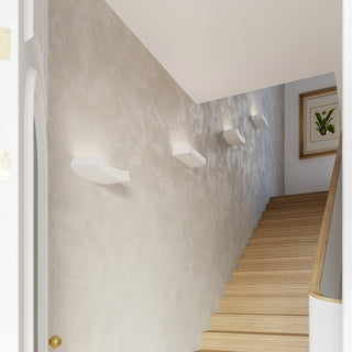 Alternating rectangular and curved ceramic wall lamps illuminating a textured staircase wall.