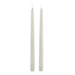 Full length view of two taupe LED dinner candles, showing illuminated wicks and ribbed bases.