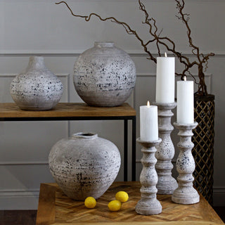 Three speckled stone vases of varying shapes and sizes displayed on wooden shelves with tall white candles.