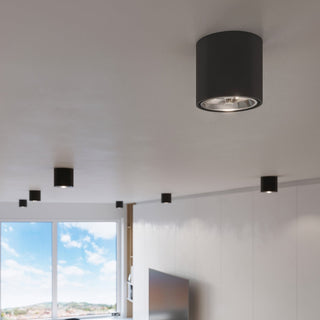 Perspective shot showing several black cylindrical lights arranged across a white ceiling near a window.