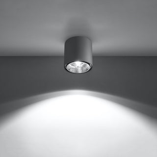 Grey cylindrical ceiling light fixture illuminated, casting a bright pool of light onto the wall below.