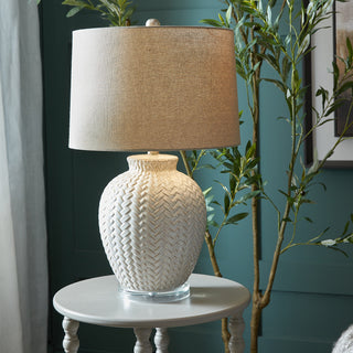 Twill weave ceramic lamp on a round side table against a teal wall, next to an olive tree.