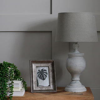 Table lamp styled on a wooden surface next to a picture frame and green trailing plant.