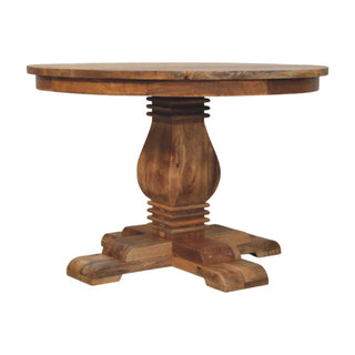 Plain front-on view of the round wooden dining table featuring a central turned pedestal base and four cross feet.