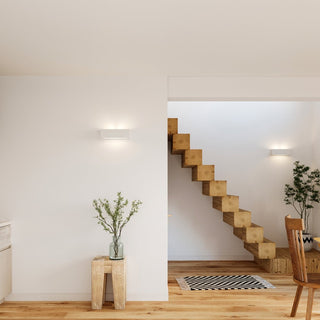 Two ceramic wall lamps installed on white walls flanking a modern staircase made of stacked wooden blocks.