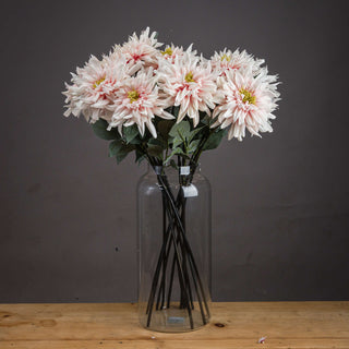 Multiple artificial pink dahlia stems arranged in a clear glass vase on a rustic wooden table.