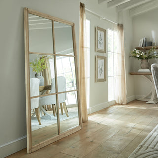 Large mirror leaning against a wall in a living space, reflecting a dining table and upholstered chairs.
