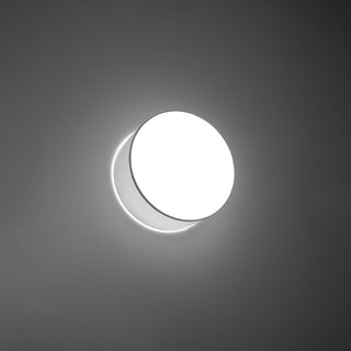 Illuminated white circular lamp showing bright crescent-shaped backlighting against a dark background.