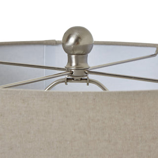 Close detail of the brushed metal finial and shade frame above the neutral linen fabric.