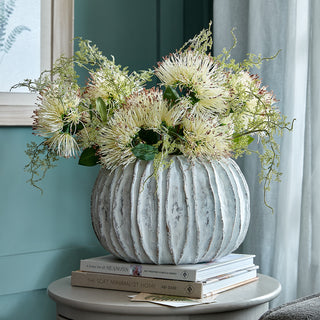 Ceramic vase filled with spiky artificial flowers, styled on a stack of books next to a teal wall.