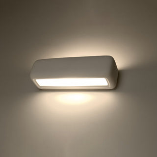 White ceramic wall lamp illuminated, showing the warm downward light cast onto the wall.