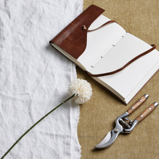 Artificial white chrysanthemum stem displayed with gardening secateurs and an open leather journal.