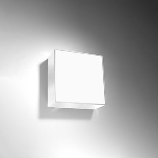 Angled view of the illuminated square white light fixture, highlighting the soft light spill onto the wall.