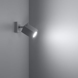 White spotlight mounted in a corner, switched on, casting a bright beam onto the adjacent wall surface.