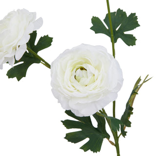 Artificial white ranunculus close-up showing the central flower detail, layered petals, and dark green leaves.