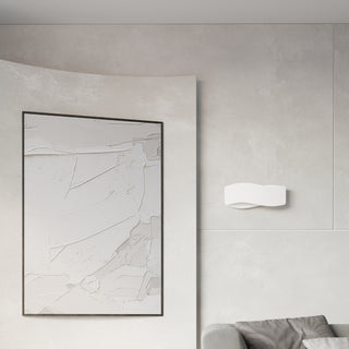 White curved wall light fixture in a minimalist room setting next to a large framed piece of textured artwork.