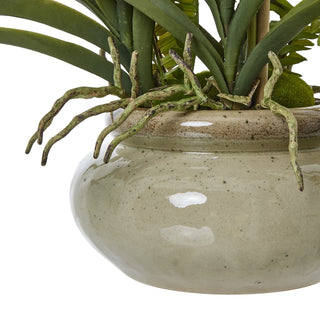 Detail of the speckled, glazed ceramic pot with a rough brown rim and artificial green roots spilling over.
