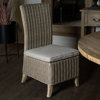 Wicker dining chair styled indoors on a dark floor, next to a round wooden table and a black planter.