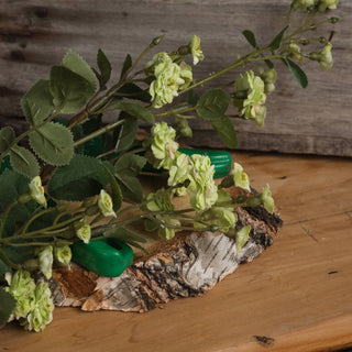 Detail shot of the artificial green meadow rose stem resting on a section of birch log slice.
